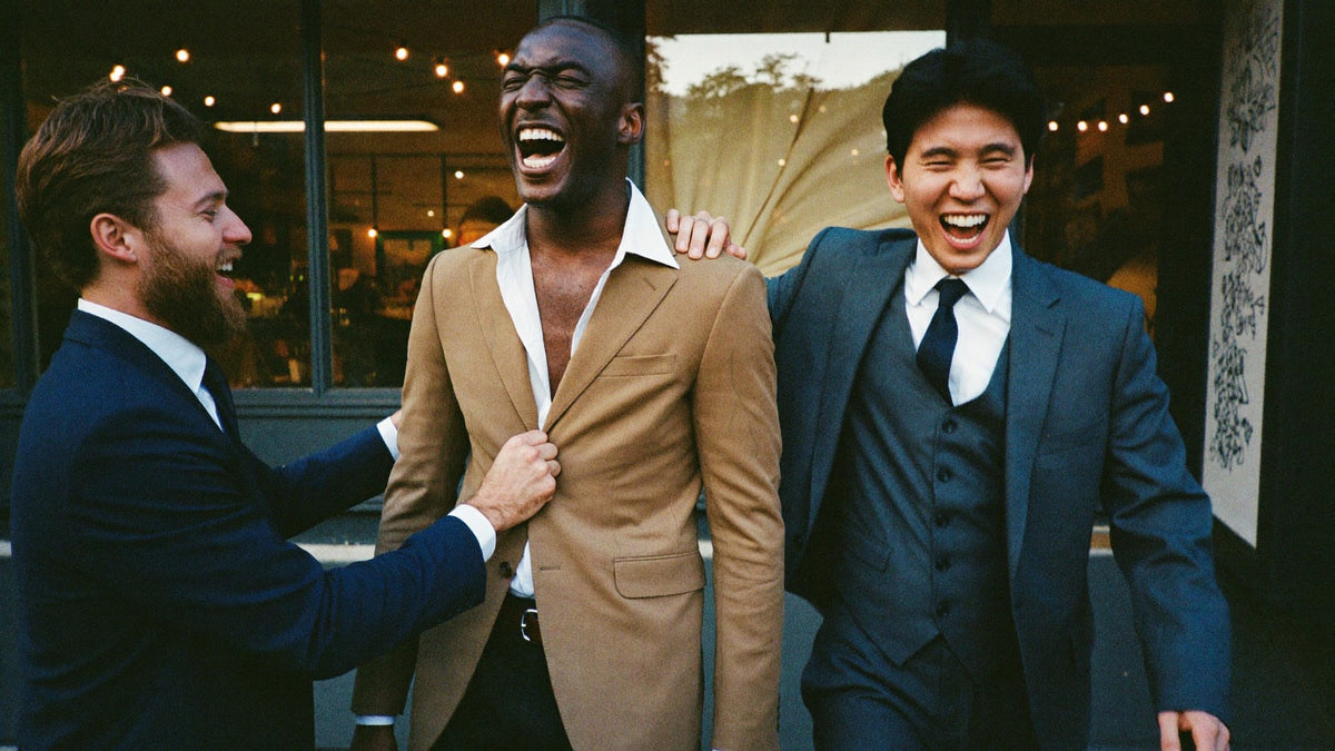 Three men in suits and blazers cracking up together outside a restaurant in the evening